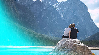 junges Paar sitzend auf Felsen vor einem Bergsee